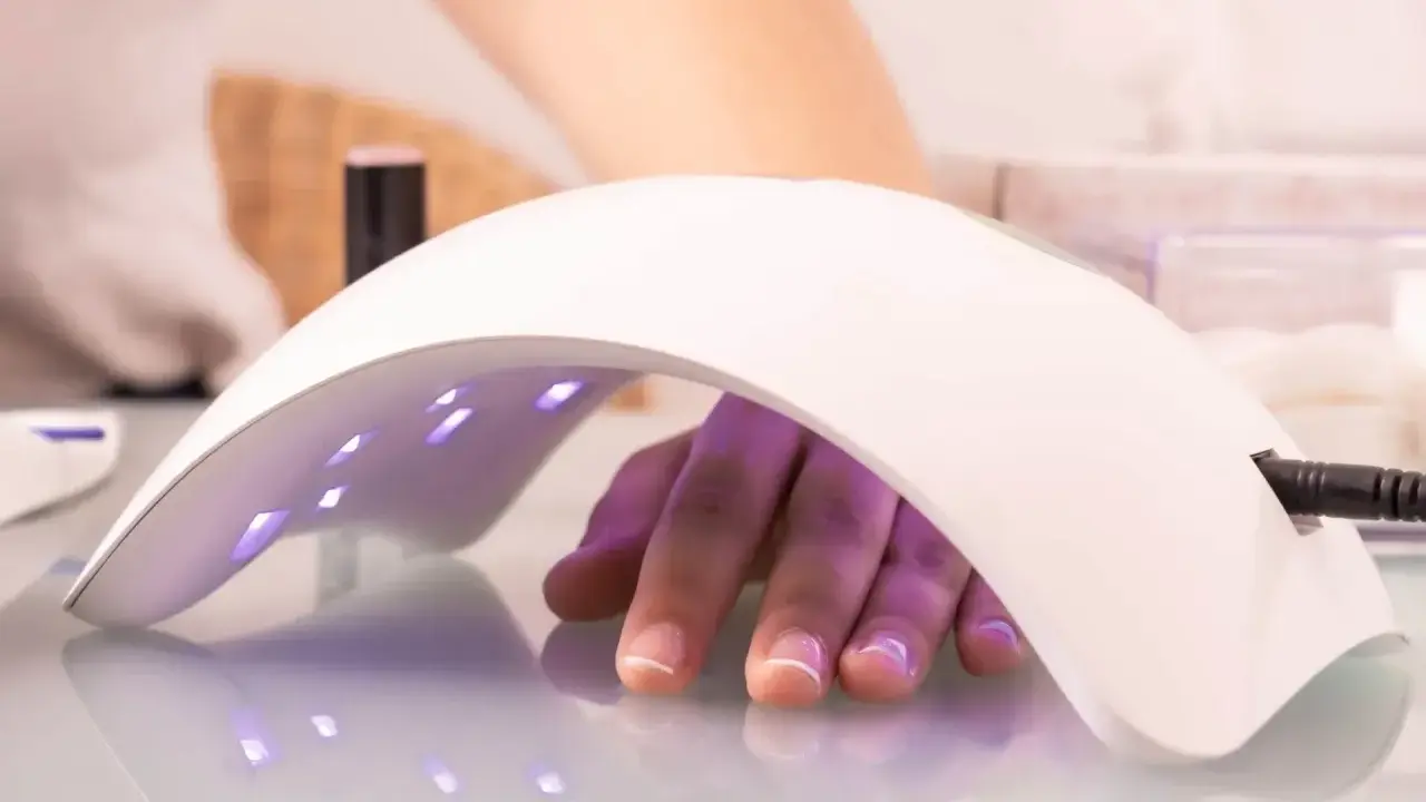 Dłoń z paznokciami pod lampą multiled, utwardzającą lakier hybrydowy.