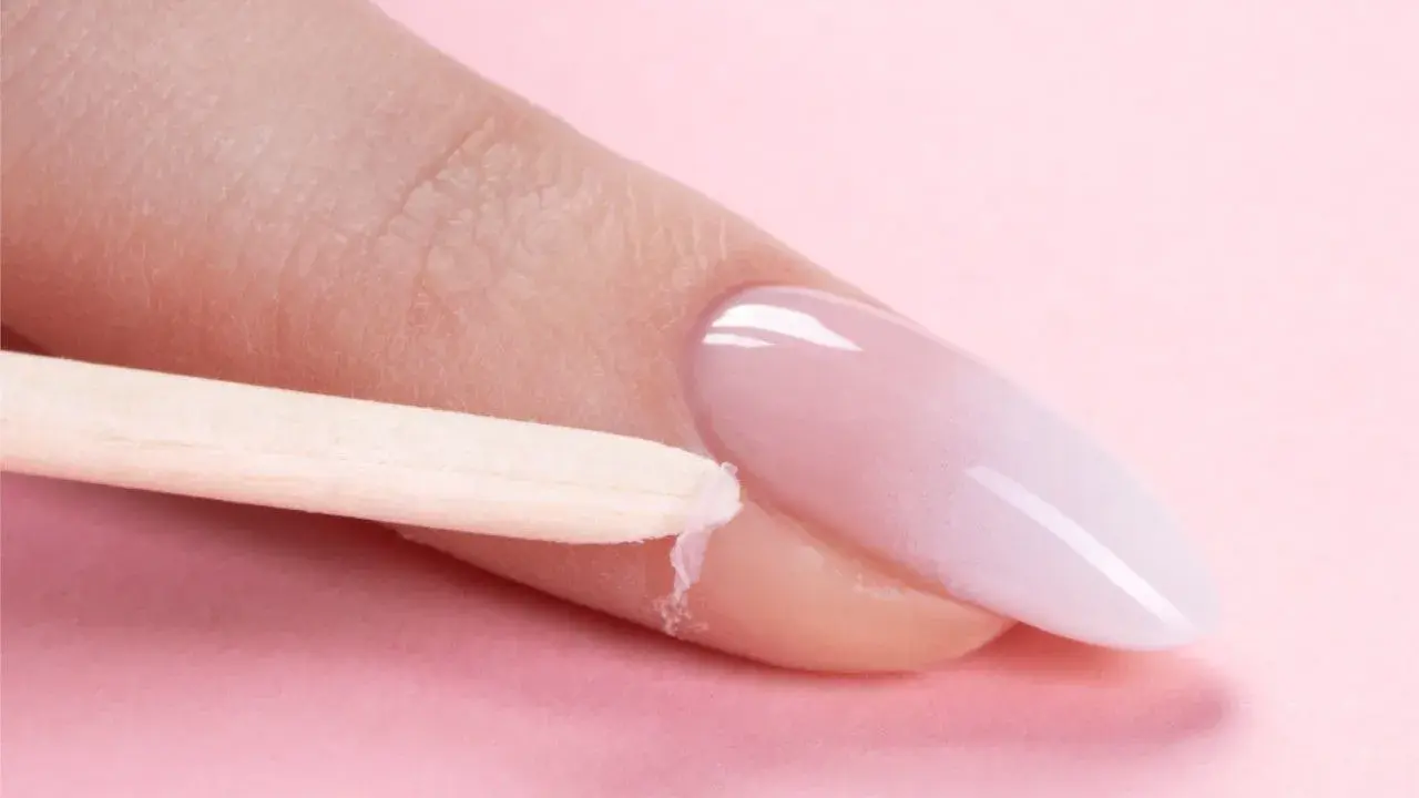 Delikatne baby boomer nails w trakcie stylizacji. Drewniany patyczek usuwa nadmiar produktu z okolicy paznokcia.