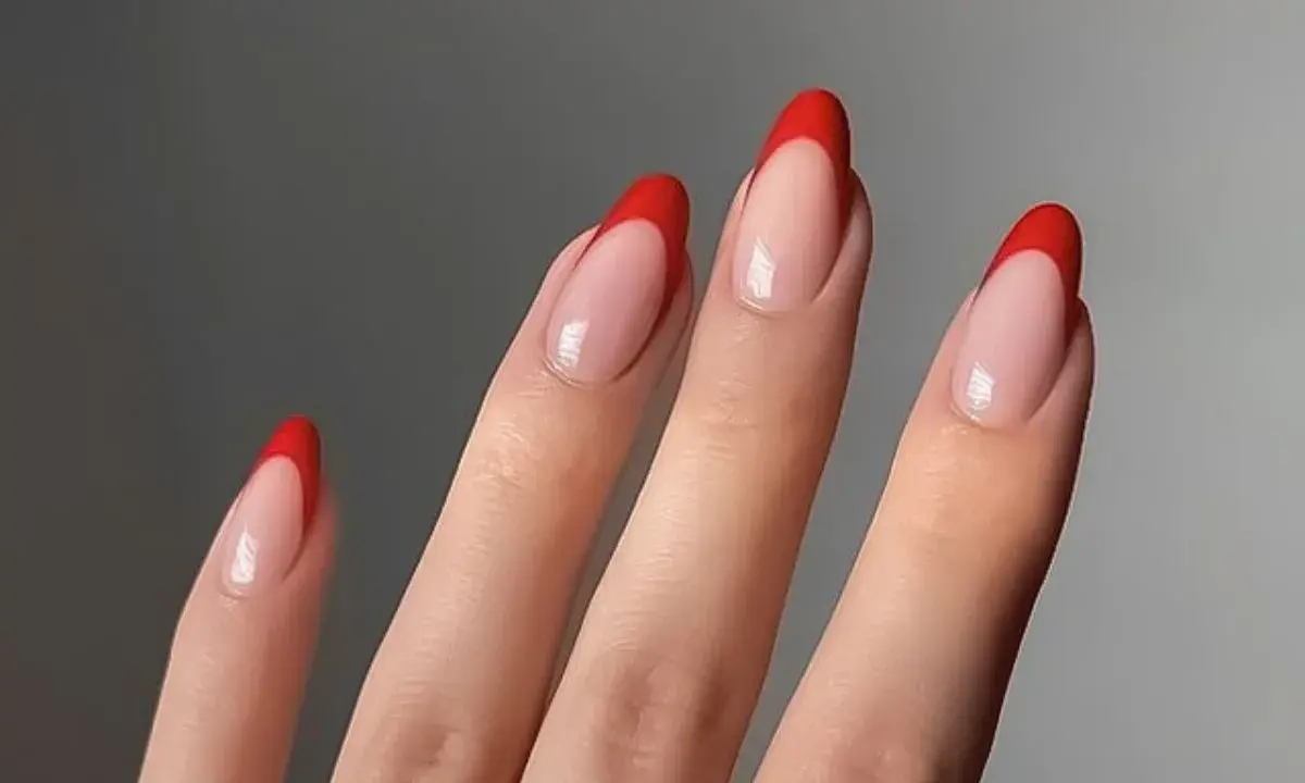 Dłonie z paznokciami w stylu czerwony french. Klasyczny manicure z wyrazistym, czerwonym akcentem na końcówkach.