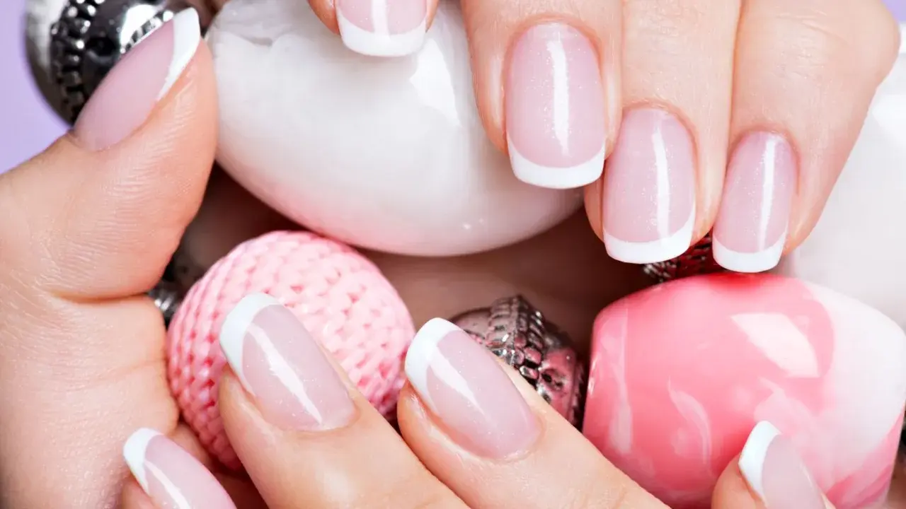 Dłonie z perfekcyjnym french manicure wykonanym lakierem hybrydowym do frencha, otoczone różowymi i białymi ozdobami.