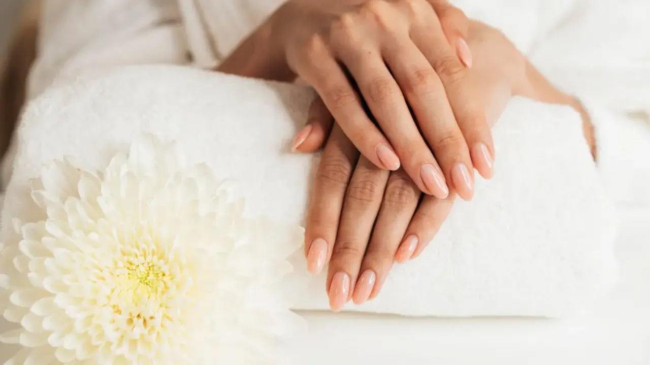 Dłonie z idealnym manicure, wykonanym przy użyciu żelu jednofazowego, na tle białego ręcznika i kwiatu.