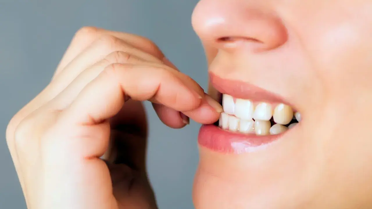 Onychofagia, czyli obgryzanie paznokci, to widoczny na zdjęciu nawyk. Dłoń zbliża się do ust, a palce są blisko zębów.