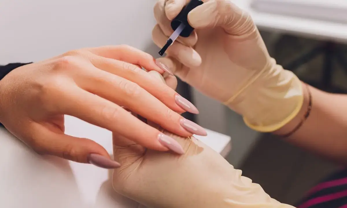 Dłonie w rękawiczkach wykonują manicure. Paznokcie w odcieniu fuksji z subtelnym frenchem.