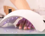 Dłoń z paznokciami pod lampą multiled, utwardzającą lakier hybrydowy.