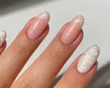 Dłoń z paznokciami w stylu francuskiego manicure z perłowym zdobieniem.