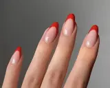 Dłonie z paznokciami w stylu czerwony french. Klasyczny manicure z wyrazistym, czerwonym akcentem na końcówkach.