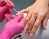 Dłonie w różowych rękawiczkach wykonują precyzyjny manicure, przygotowując paznokcie na letnie kolory.