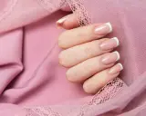 Dłoń z klasycznym french manicure, prezentująca różne rodzaje frencha na tle pudrowej koronki.