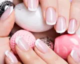 Dłonie z perfekcyjnym french manicure wykonanym lakierem hybrydowym do frencha, otoczone różowymi i białymi ozdobami.