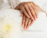 Dłonie z idealnym manicure, wykonanym przy użyciu żelu jednofazowego, na tle białego ręcznika i kwiatu.