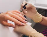 Dłonie w rękawiczkach wykonują manicure. Paznokcie w odcieniu fuksji z subtelnym frenchem.