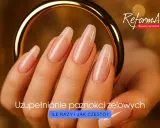 Dłoń z idealnie wykonanymi paznokciami żelowymi, prezentującymi prawidłową budowę. Złota obręcz podkreśla elegancję.