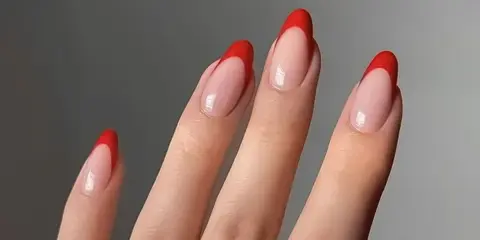 Dłonie z paznokciami w stylu czerwony french. Klasyczny manicure z wyrazistym, czerwonym akcentem na końcówkach.