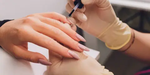 Dłonie w rękawiczkach wykonują manicure. Paznokcie w odcieniu fuksji z subtelnym frenchem.