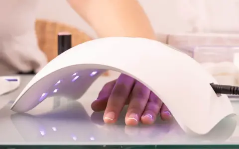 Dłoń z paznokciami pod lampą multiled, utwardzającą lakier hybrydowy.
