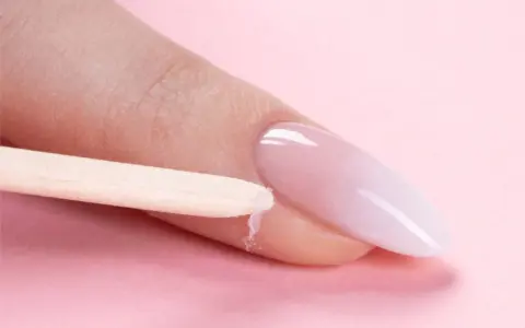 Delikatne baby boomer nails w trakcie stylizacji. Drewniany patyczek usuwa nadmiar produktu z okolicy paznokcia.