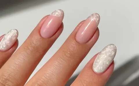 Dłoń z paznokciami w stylu francuskiego manicure z perłowym zdobieniem.