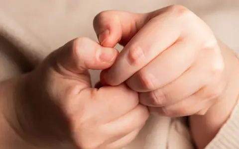 Dłonie splatają się, ukazując delikatny obłączek paznokcia na jednym z palców.