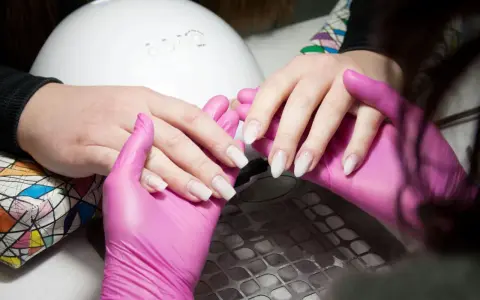 Dłonie w różowych rękawiczkach przygotowują paznokcie do stylizacji. Długość paznokci jest idealna do stworzenia pięknego manicure.