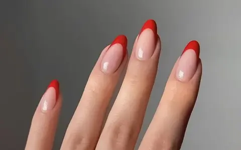 Dłonie z paznokciami w stylu czerwony french. Klasyczny manicure z wyrazistym, czerwonym akcentem na końcówkach.