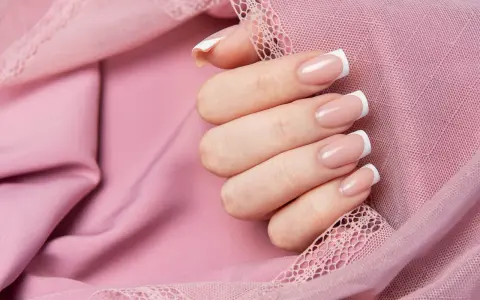 Dłoń z klasycznym french manicure, prezentująca różne rodzaje frencha na tle pudrowej koronki.