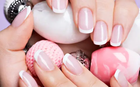 Dłonie z perfekcyjnym french manicure wykonanym lakierem hybrydowym do frencha, otoczone różowymi i białymi ozdobami.