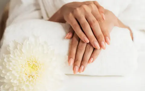 Dłonie z idealnym manicure, wykonanym przy użyciu żelu jednofazowego, na tle białego ręcznika i kwiatu.