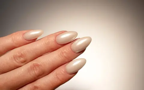 Dłoń z paznokciami w kształcie migdała, pomalowanymi na perłowy beż. Idealna krzywa C podkreśla elegancję manicure.