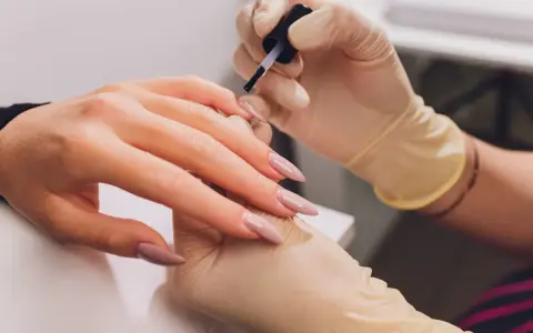 Dłonie w rękawiczkach wykonują manicure. Paznokcie w odcieniu fuksji z subtelnym frenchem.