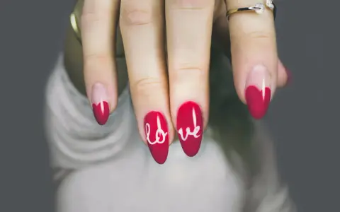 Dłoń z paznokciami w kształcie serca i napisem "love". Różne rodzaje paznokci, od klasycznych po te z ozdobami.