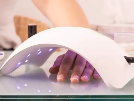 Dłoń z paznokciami pod lampą multiled, utwardzającą lakier hybrydowy.