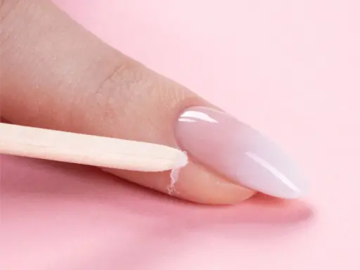Delikatne baby boomer nails w trakcie stylizacji. Drewniany patyczek usuwa nadmiar produktu z okolicy paznokcia.