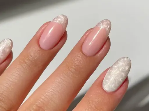 Dłoń z paznokciami w stylu francuskiego manicure z perłowym zdobieniem.