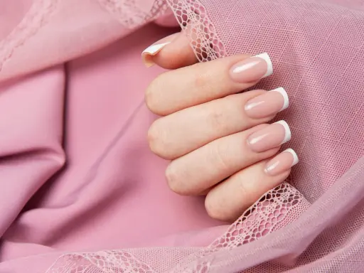 Dłoń z klasycznym french manicure, prezentująca różne rodzaje frencha na tle pudrowej koronki.