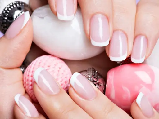 Dłonie z perfekcyjnym french manicure wykonanym lakierem hybrydowym do frencha, otoczone różowymi i białymi ozdobami.