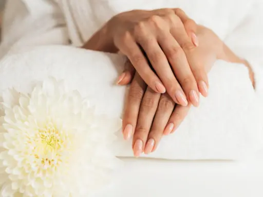 Dłonie z idealnym manicure, wykonanym przy użyciu żelu jednofazowego, na tle białego ręcznika i kwiatu.