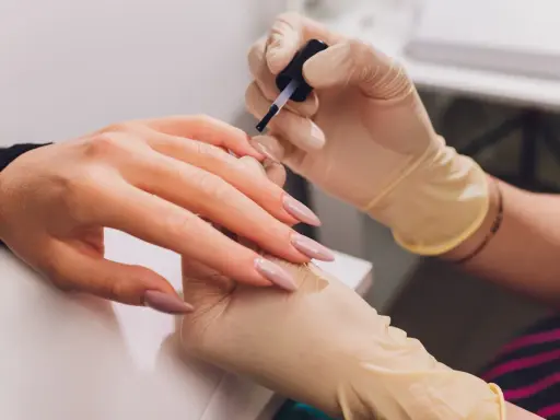 Dłonie w rękawiczkach wykonują manicure. Paznokcie w odcieniu fuksji z subtelnym frenchem.