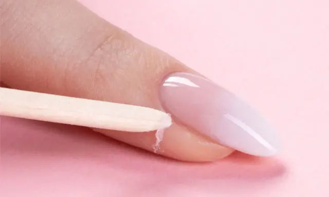 Delikatne baby boomer nails w trakcie stylizacji. Drewniany patyczek usuwa nadmiar produktu z okolicy paznokcia.