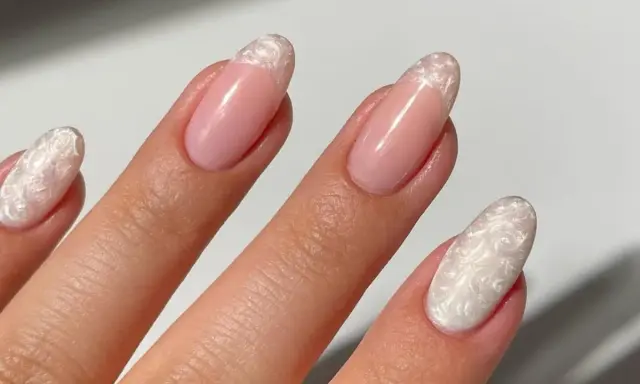 Dłoń z paznokciami w stylu francuskiego manicure z perłowym zdobieniem.