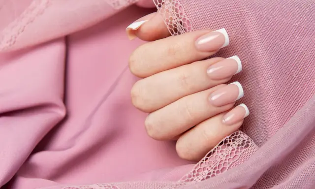 Dłoń z klasycznym french manicure, prezentująca różne rodzaje frencha na tle pudrowej koronki.