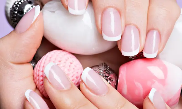 Dłonie z perfekcyjnym french manicure wykonanym lakierem hybrydowym do frencha, otoczone różowymi i białymi ozdobami.