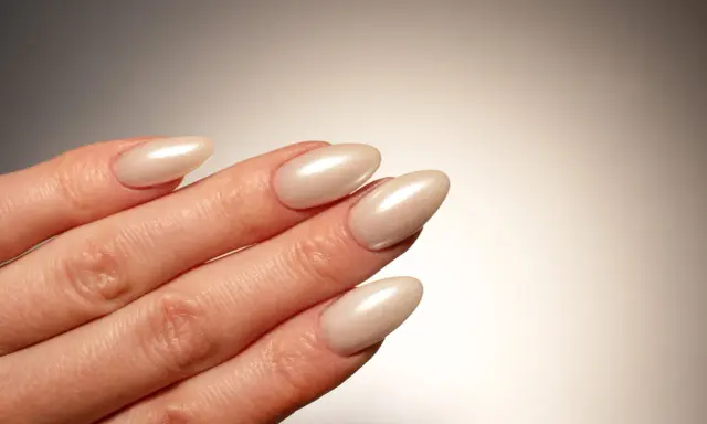Dłoń z paznokciami w kształcie migdała, pomalowanymi na perłowy beż. Idealna krzywa C podkreśla elegancję manicure.