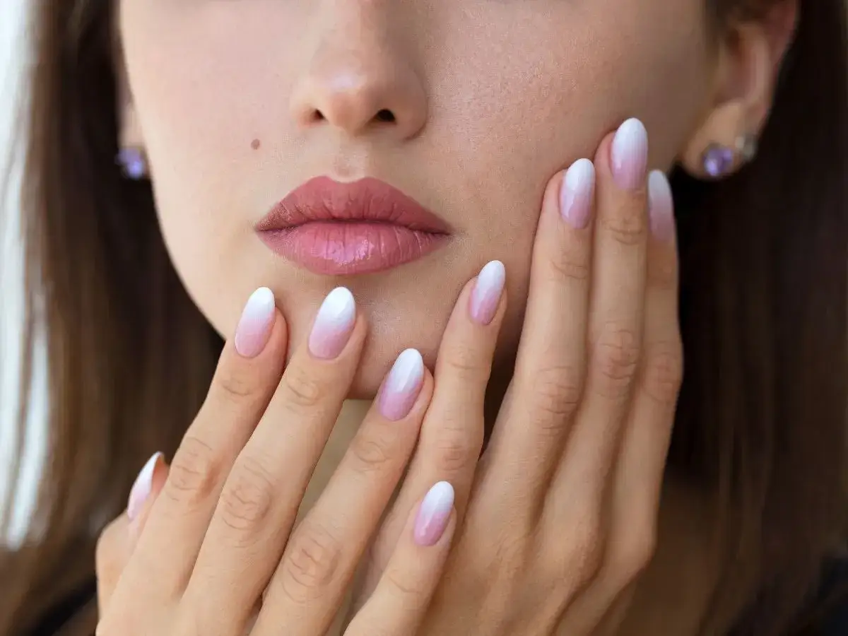 Delikatne baby boomer nails na dłoniach, podkreślające subtelny makijaż ust.