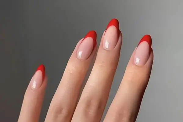 Dłonie z paznokciami w stylu czerwony french. Klasyczny manicure z wyrazistym, czerwonym akcentem na końcówkach.